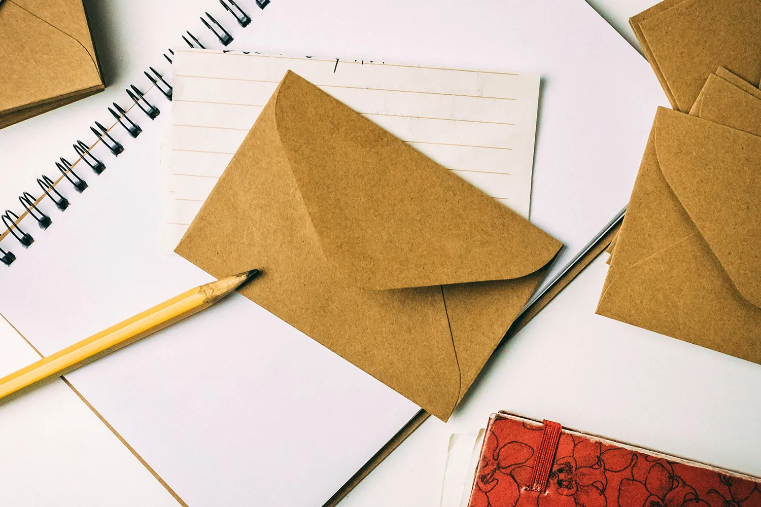 textpiber-schreibmethoden-leon-rojas-unsplash Ein braunes Briefkuvert liegt im Mittelpunkt des Bildes. Draunter und rundherum liegen Schreibuntensilien.